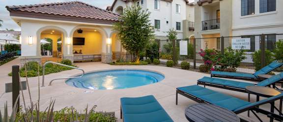 A pool surrounded by lounge chairs and a building in the background.