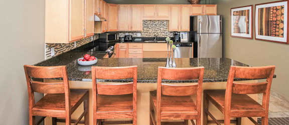 A kitchen with a granite countertop and wooden chairs.