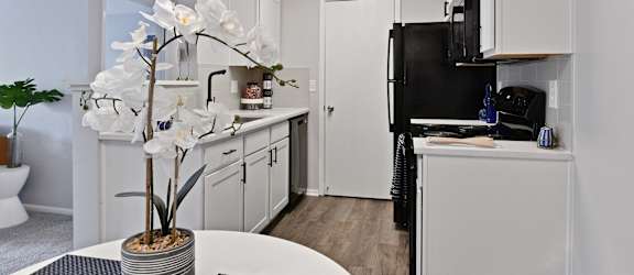 a kitchen with white cabinets and a black refrigerator and a table with a vase
