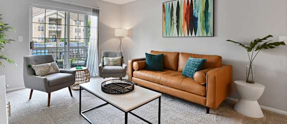 A bright and modern living room with a brown couch, a grey armchair, and a white coffee table.