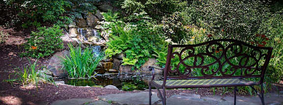a bench sits on a stone patio next to a pondat Monroeville Apartments, Pennslyvania, 15146