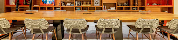 A room with a long table and chairs in front of a shelf with various items on it.