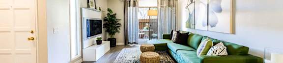 Living room with large green couch and sliding glass patio doors in background at CASA GRANDE APARTMENT HOMES, California
