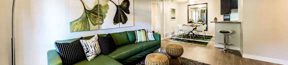 Living room with modern lighting and big green couch with  dining room and breakfast bar in background at CASA GRANDE APARTMENT HOMES, Cypress, California