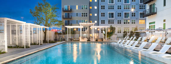 a swimming pool with white chaise lounge chairs and an apartment building in the background