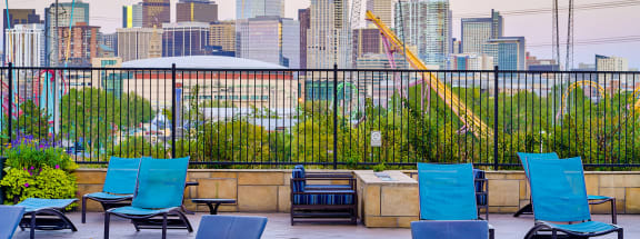 an outdoor pool with blue lounge chairs and a fire pit with a view of the city skyline