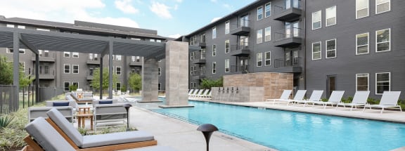 a swimming pool with lounge chairs and tables next to an apartment building