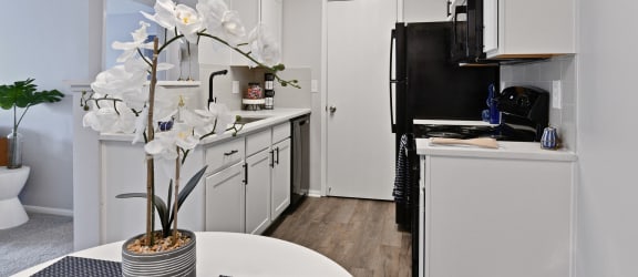 a kitchen with white cabinets and a black refrigerator and a table with a vase