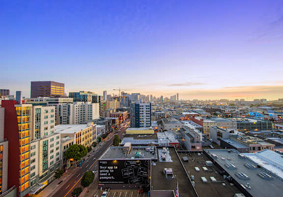 A rooftop patio with a bench and a table with a view of the city at sunset.