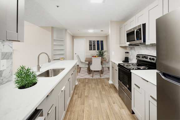 an open kitchen and living room with white cabinets and stainless steel appliances