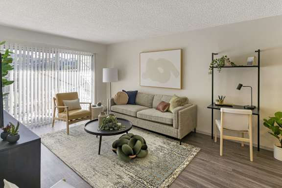 A living room with a grey couch, a coffee table, a chair, a potted plant, and a shelf with a plant on it.
