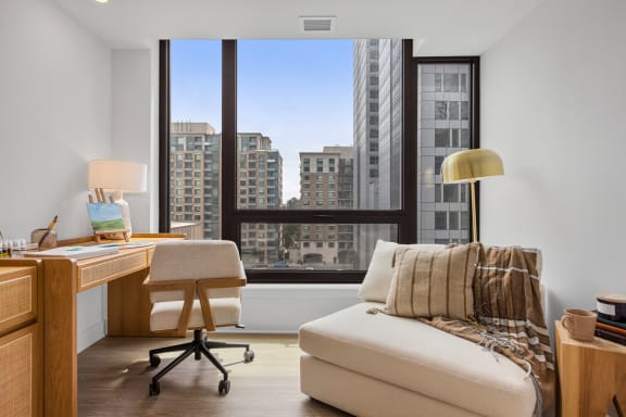 a living room with a large window and a desk with a chair and a couch