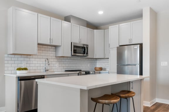 a kitchen with white cabinets and a white island with two stools