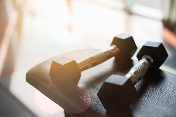 A pair of black dumbbells resting on a black mat.