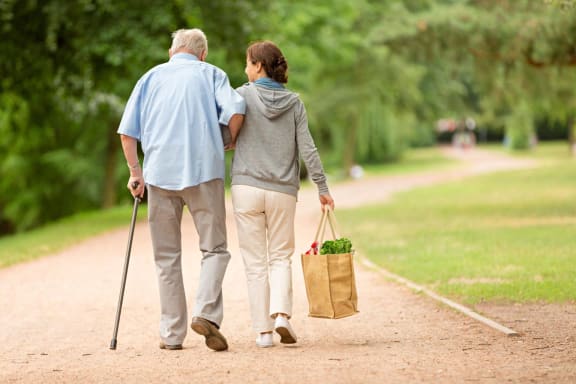 an elderly man and woman walking down a path with a bag and cane