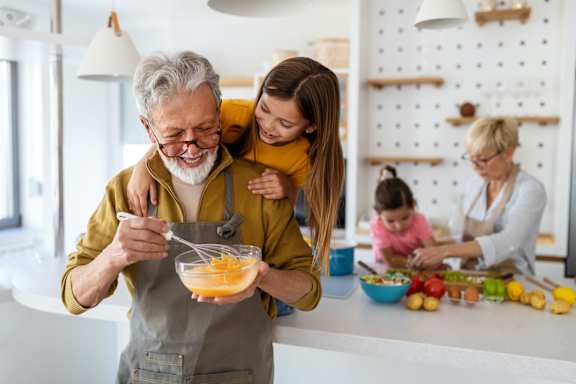 an older man and woman cooking in the kitchen with their granddaughter and granddaughter in the background