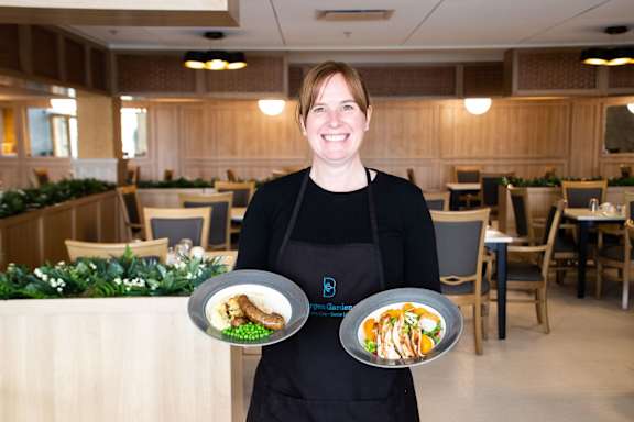 a woman in an apron holding two plates of food