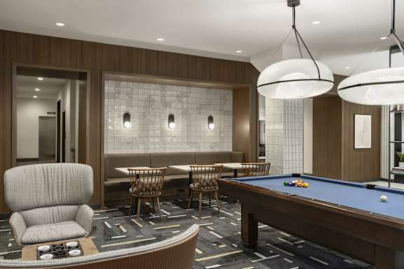 A pool table is surrounded by chairs in a room with a wood panelled wall.