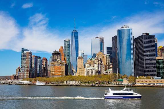 A boat is sailing in front of a city skyline. at Aria, New York, NY