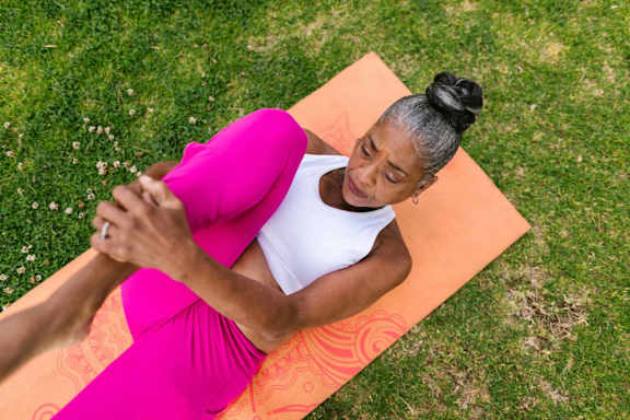 A woman in a pink dress is sitting on a yoga mat outdoors.