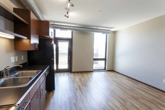 an empty living room with a kitchen and a door to a balcony