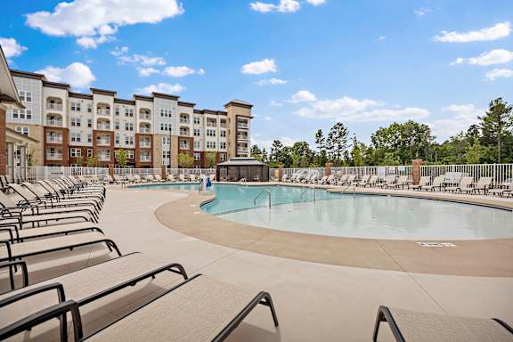 A large swimming pool surrounded by lounge chairs in front of apartment buildings.