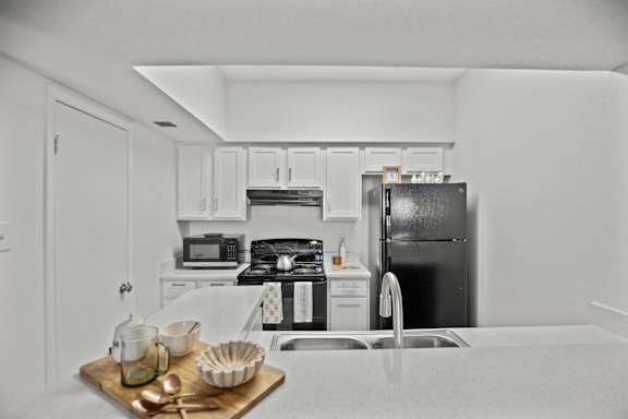 A kitchen with a black refrigerator and white cabinets.