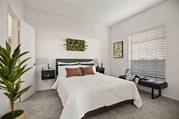 A bedroom with a large bed, a potted plant, and a bench.