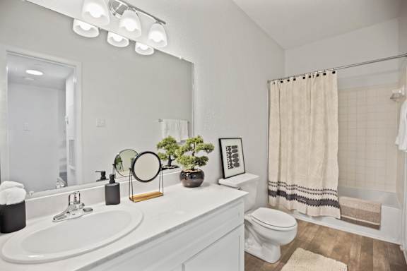 A bathroom with a white sink, toilet, and a mirror with lights above it.