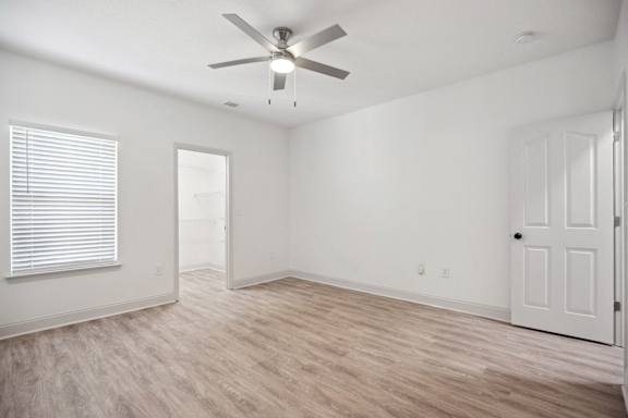 A room with a ceiling fan and light, hardwood floors, and white walls with a door and window.