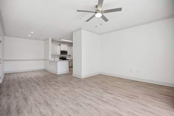 A room with a ceiling fan and light fixture, and a kitchenette in the background.