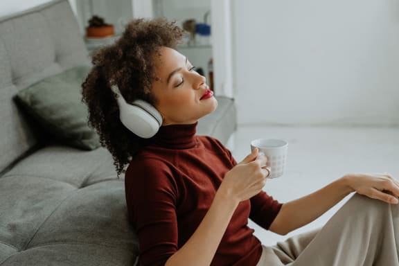 a woman sitting on a couch with headphones on and holding a cup of coffee at Proximity at ODU, Norfolk, Virginia