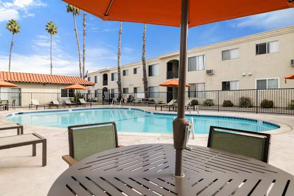 A pool area with a table and chairs under an umbrella.