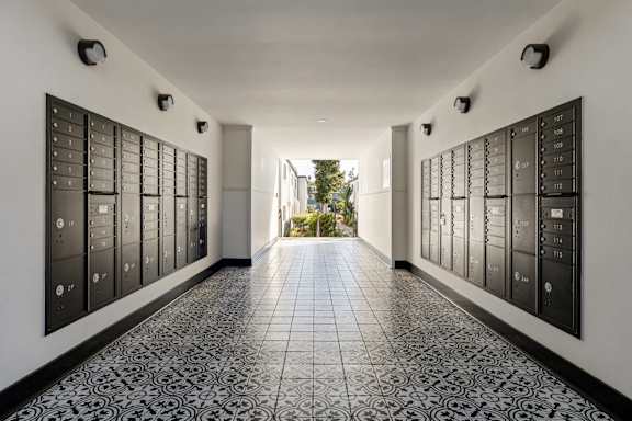 A long hallway with black and white tiles and a black wall with many mailboxes.