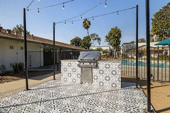 A black and white tiled outdoor kitchen area with a grill and a pool in the background.