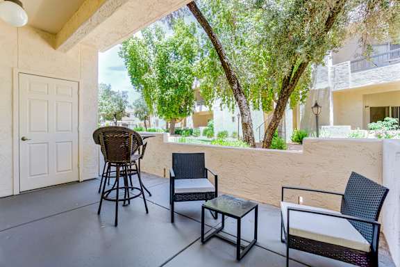 A patio with a chair, table and a view of a tree and building.