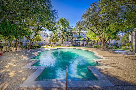 A swimming pool surrounded by trees and a building in the background.