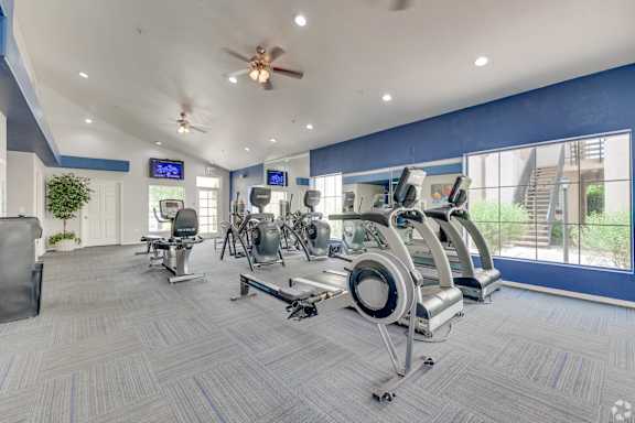A gym with a variety of exercise equipment and a ceiling fan.
