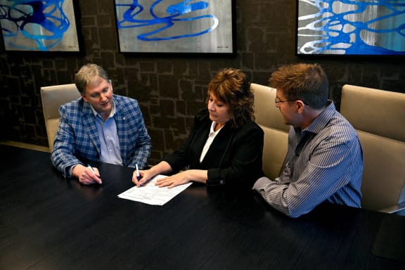 a group of people sitting around a table signing a piece of paper