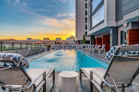 A pool area with lounge chairs and a view of the city skyline at sunset.