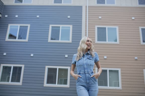 A woman in a denim jumpsuit stands in front of a building.