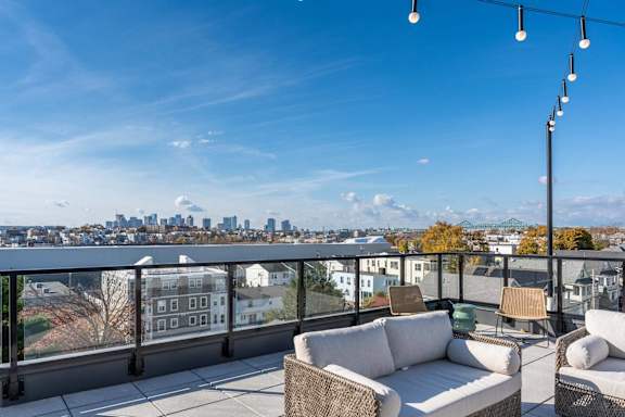 A balcony with a white couch and a chair with a city view in the background.