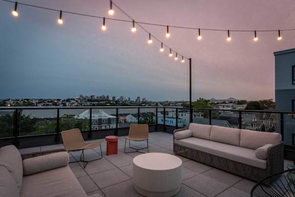 A patio with a couch, chairs, and a table with string lights above.