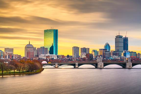 A city skyline at sunset with a river in the foreground.