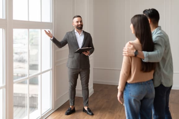 a man in a suit stands in an empty room with a tablet and a woman in a