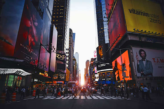 A busy city street with people crossing the road and tall buildings on either side.