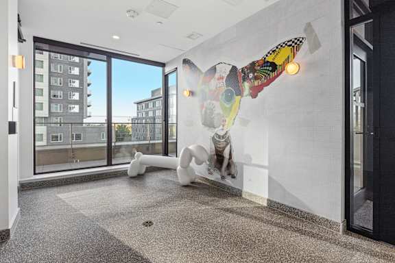 A white sculpture of a person with a colorful patterned head is on a wall in a room with a view of a building outside.