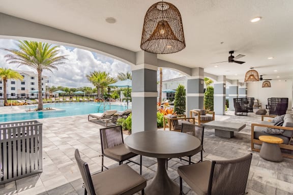 a resident clubhouse with tables and chairs and a pool in the background at Edge75, Naples, FL, 34104