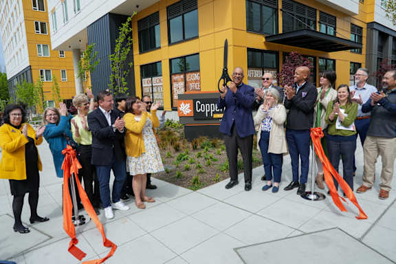 A group of people are gathered in front of a building with a sign that reads "Copper.".