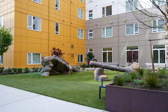 A large rock sits in a grassy area in front of a yellow building.